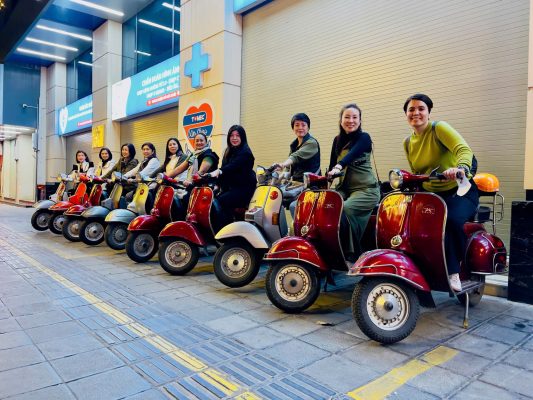 Female tour guide leading Vespa group through bustling street scenes